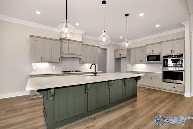 kitchen featuring built in microwave, sink, decorative light fixtures, gray cabinets, and a kitchen island with sink