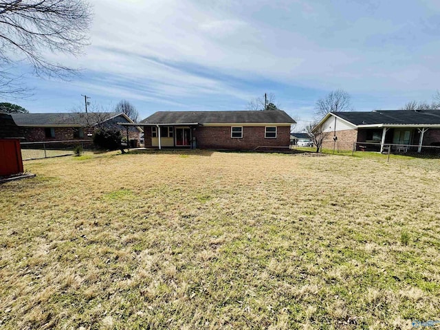 rear view of house with brick siding, fence, and a yard