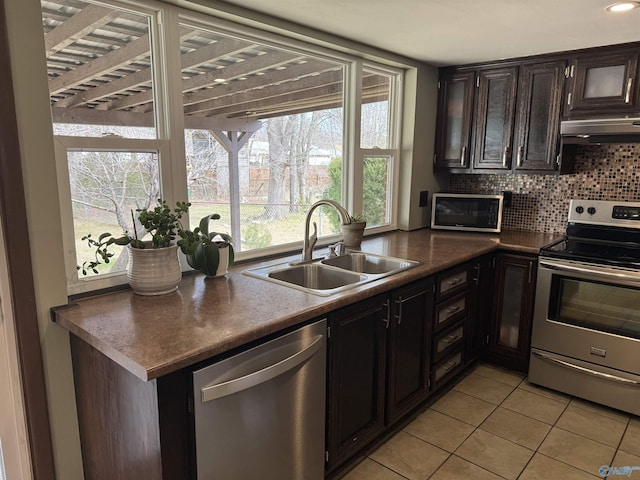 kitchen with light tile patterned floors, stainless steel appliances, dark countertops, backsplash, and a sink