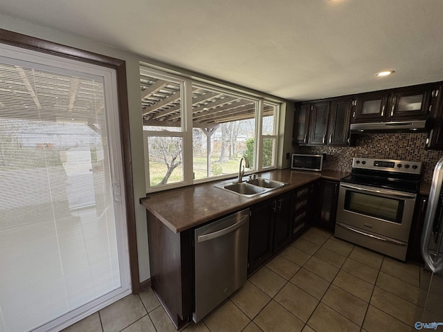 kitchen featuring dark countertops, appliances with stainless steel finishes, a sink, tile patterned flooring, and under cabinet range hood