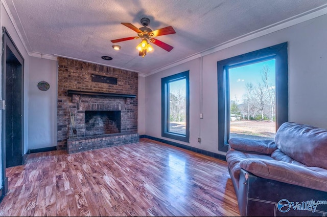 living room with a brick fireplace, ornamental molding, a textured ceiling, ceiling fan, and hardwood / wood-style floors