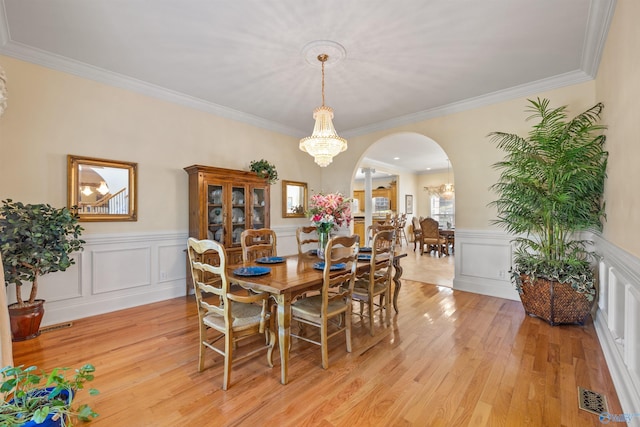 dining room with arched walkways, light wood-type flooring, visible vents, and an inviting chandelier