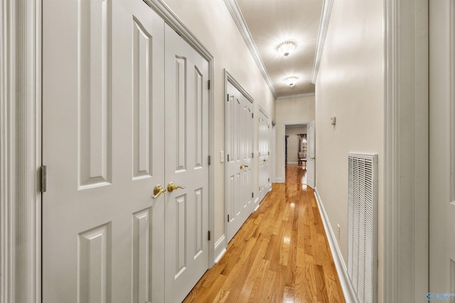 corridor with baseboards, ornamental molding, visible vents, and light wood-style floors