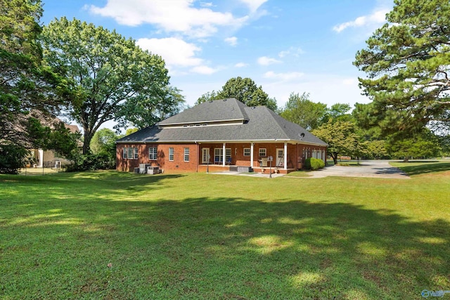 back of house with brick siding, a lawn, and driveway