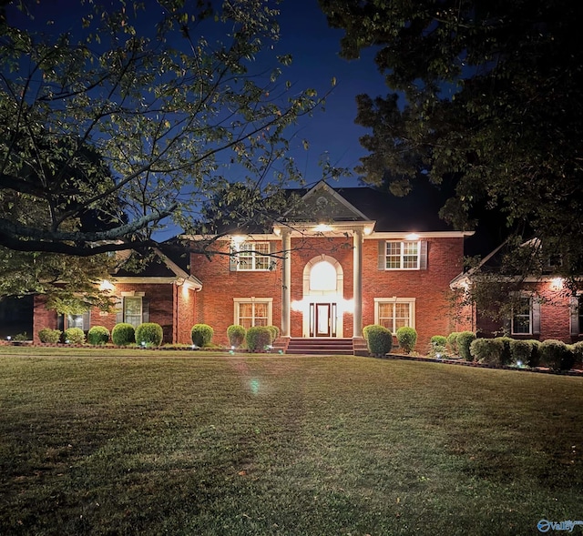 neoclassical home featuring brick siding and a yard