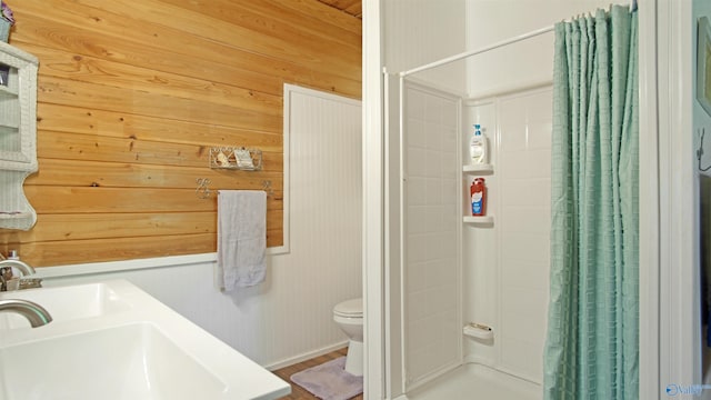 bathroom featuring curtained shower, wood walls, dual sinks, and toilet