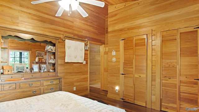 unfurnished bedroom with multiple closets, wood walls, ceiling fan, and dark hardwood / wood-style floors