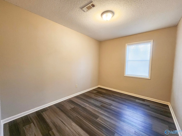 empty room with dark wood finished floors, baseboards, visible vents, and a textured ceiling