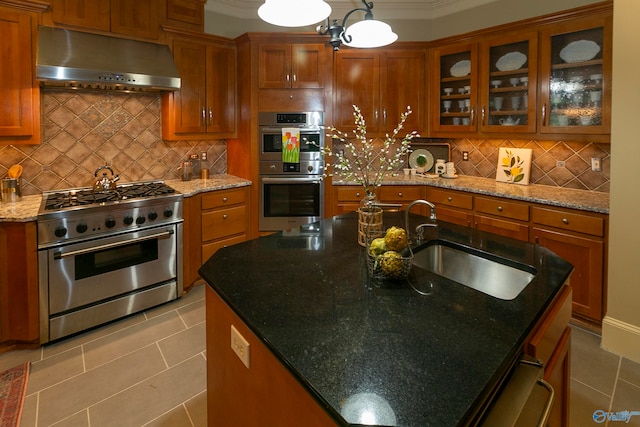 kitchen with light tile patterned flooring, wall chimney range hood, stainless steel appliances, decorative backsplash, and an island with sink