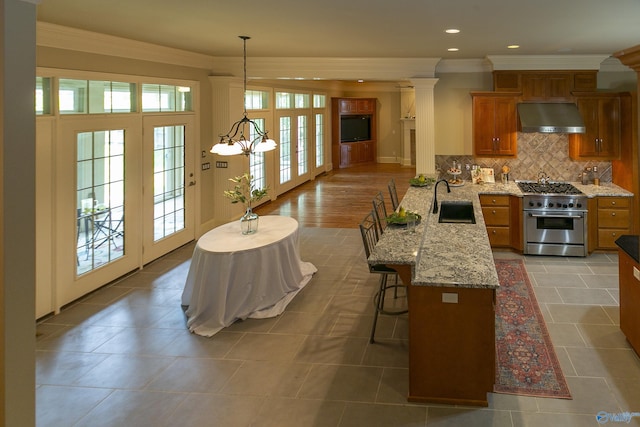 kitchen with brown cabinetry, decorative backsplash, ventilation hood, high end stove, and a sink