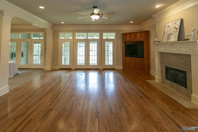 unfurnished living room with a healthy amount of sunlight, crown molding, wood finished floors, and a tile fireplace