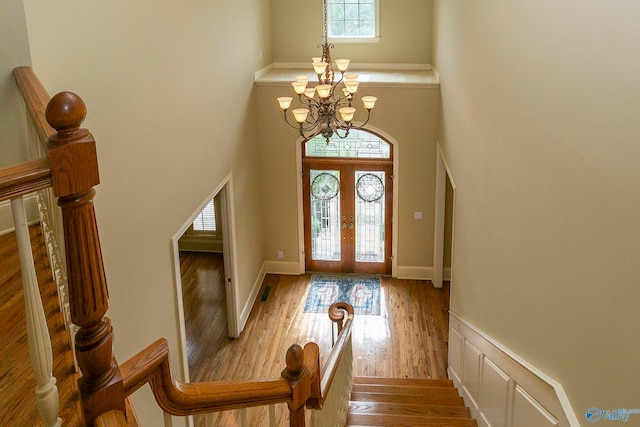 entrance foyer featuring wood-type flooring, a notable chandelier, a towering ceiling, and plenty of natural light