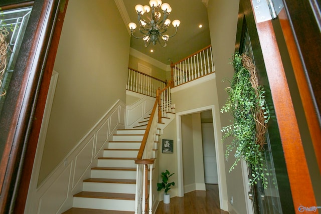 stairway featuring ornamental molding, an inviting chandelier, wood-type flooring, and a high ceiling