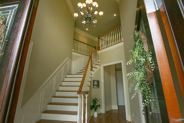 stairway featuring a high ceiling, ornamental molding, wood finished floors, a chandelier, and baseboards