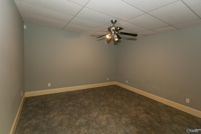 empty room with a drop ceiling, dark carpet, baseboards, and ceiling fan