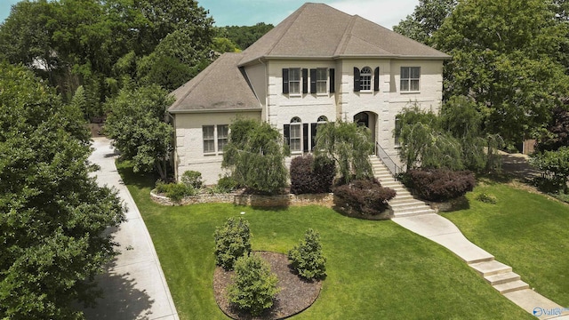 french country inspired facade featuring roof with shingles, a front lawn, stairway, and brick siding