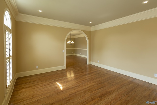 spare room with arched walkways, ornamental molding, wood finished floors, and baseboards