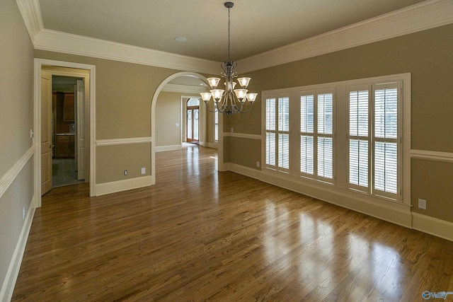 unfurnished dining area featuring baseboards, arched walkways, ornamental molding, wood finished floors, and a notable chandelier