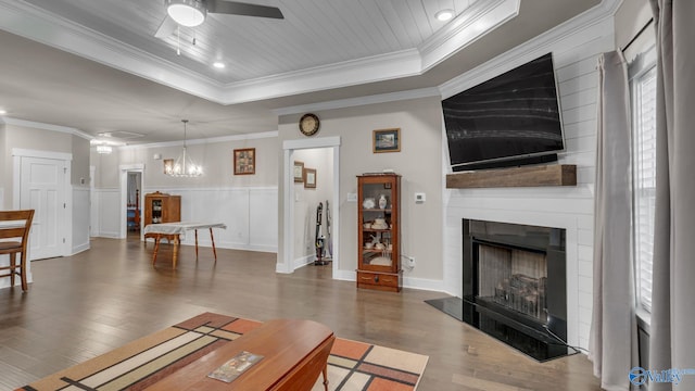 living room with a large fireplace, ceiling fan, crown molding, wainscoting, and wood finished floors
