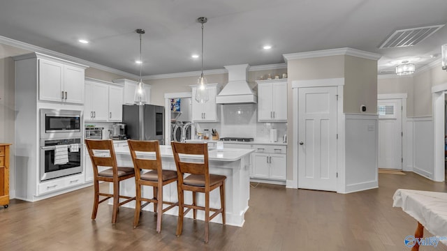kitchen featuring a breakfast bar area, stainless steel appliances, light countertops, visible vents, and premium range hood
