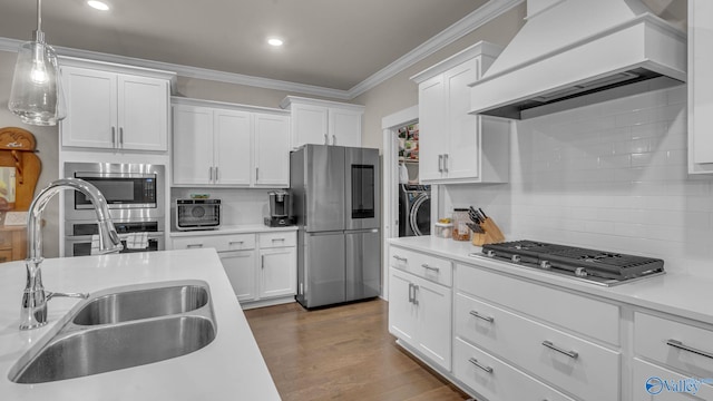 kitchen with tasteful backsplash, appliances with stainless steel finishes, a sink, white cabinetry, and premium range hood
