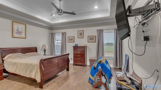 bedroom featuring light wood-type flooring, multiple windows, ornamental molding, and a tray ceiling