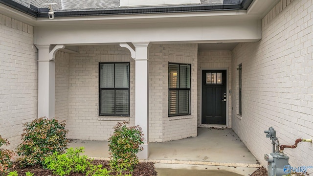 doorway to property with a porch, a shingled roof, and brick siding
