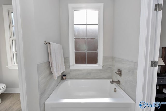 bathroom with a tub to relax in and toilet