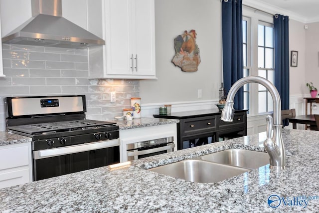 kitchen with white cabinets, sink, gas range, wall chimney exhaust hood, and light stone counters