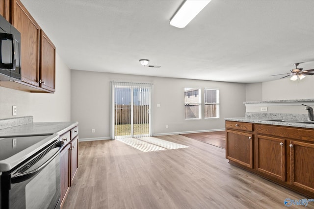 kitchen featuring stainless steel appliances, light stone counters, sink, ceiling fan, and light hardwood / wood-style flooring