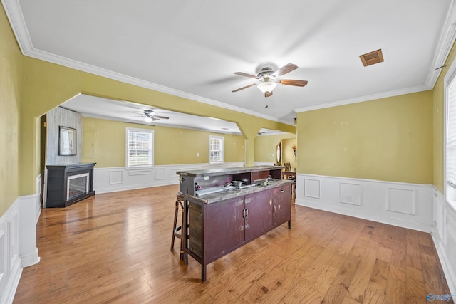 kitchen with ornamental molding, light hardwood / wood-style flooring, a kitchen breakfast bar, ceiling fan, and a center island