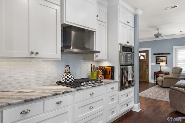 kitchen with wall chimney exhaust hood, dark wood-type flooring, backsplash, white cabinetry, and appliances with stainless steel finishes