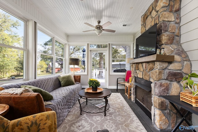 sunroom / solarium with wood ceiling, ceiling fan, a stone fireplace, and plenty of natural light