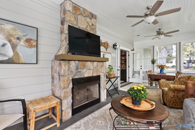 living room with a stone fireplace, wood walls, wooden ceiling, and ceiling fan