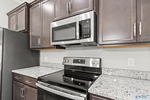 kitchen with dark brown cabinets, appliances with stainless steel finishes, and light stone countertops