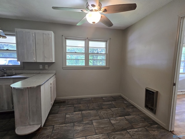 kitchen with baseboards, heating unit, light countertops, a sink, and white cabinetry