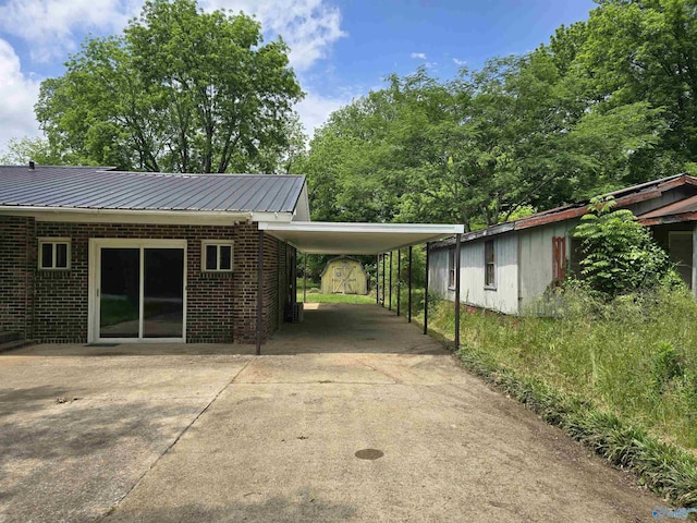 view of home's exterior with brick siding, driveway, metal roof, and an attached carport
