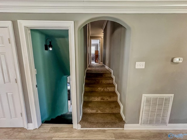 staircase featuring arched walkways, wood finished floors, visible vents, baseboards, and ornamental molding