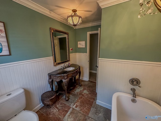 bathroom featuring a wainscoted wall, crown molding, a freestanding bath, toilet, and a sink