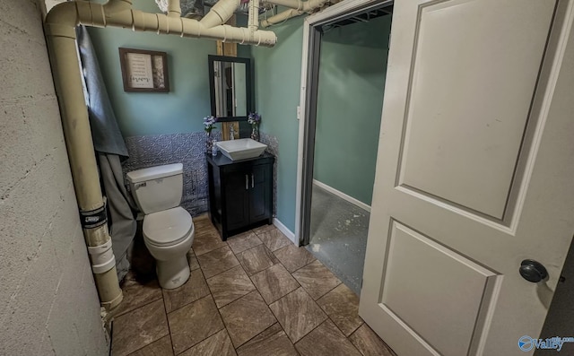 half bath featuring baseboards, vanity, and toilet