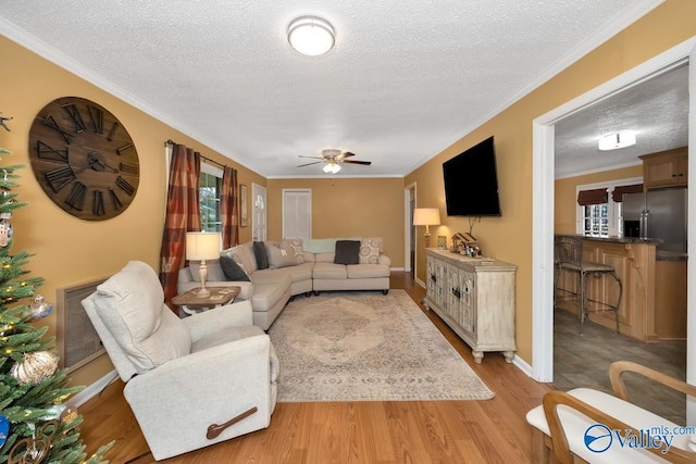 living room with light wood-type flooring, a textured ceiling, and ornamental molding