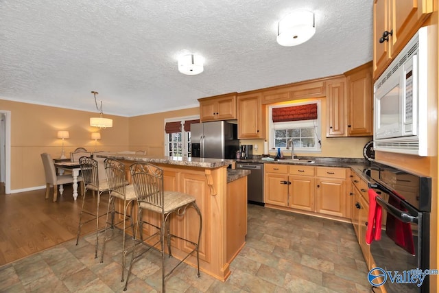 kitchen featuring plenty of natural light, sink, appliances with stainless steel finishes, decorative light fixtures, and a breakfast bar area