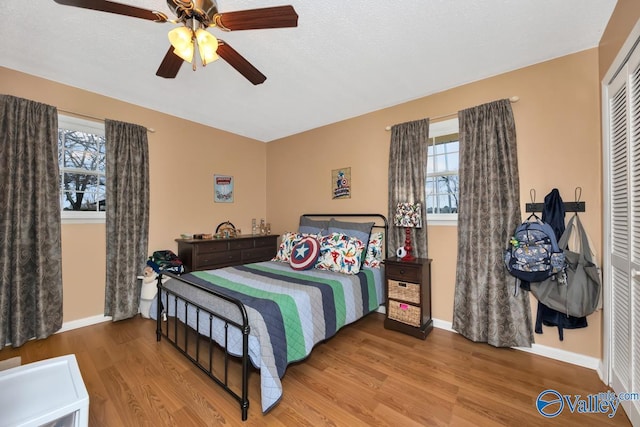 bedroom with hardwood / wood-style floors, ceiling fan, multiple windows, and a closet