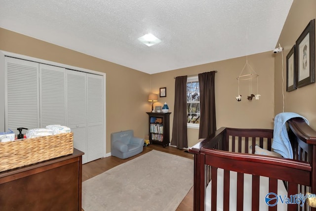 bedroom featuring hardwood / wood-style floors, a crib, a textured ceiling, and a closet