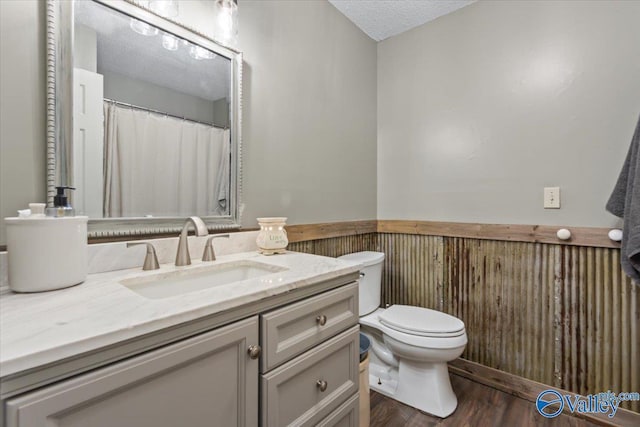 bathroom featuring hardwood / wood-style flooring, wooden walls, vanity, a textured ceiling, and toilet