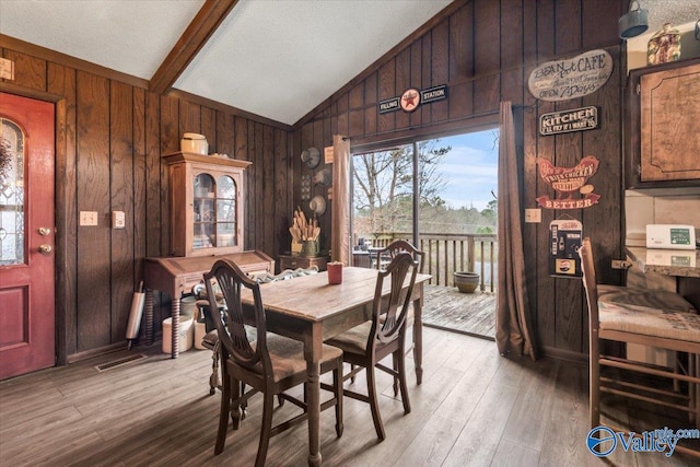 dining space with light hardwood / wood-style floors, lofted ceiling with beams, and wood walls