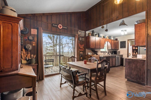 dining space featuring sink, vaulted ceiling, a textured ceiling, wooden walls, and light hardwood / wood-style floors