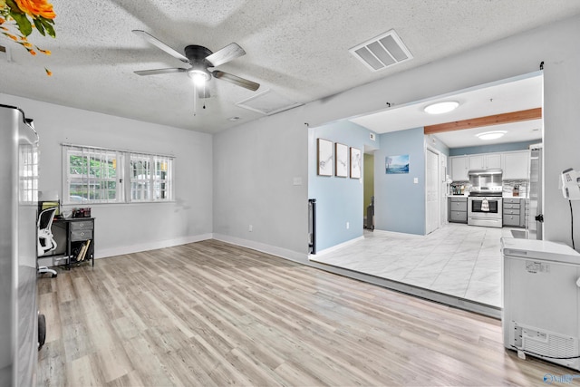 unfurnished living room featuring ceiling fan, light wood-style floors, a textured ceiling, baseboards, and visible vents