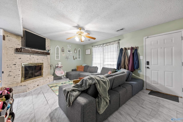living room featuring visible vents, marble finish floor, a brick fireplace, a textured ceiling, and a ceiling fan