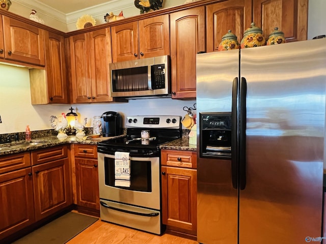 kitchen with sink, crown molding, light wood-type flooring, appliances with stainless steel finishes, and dark stone counters